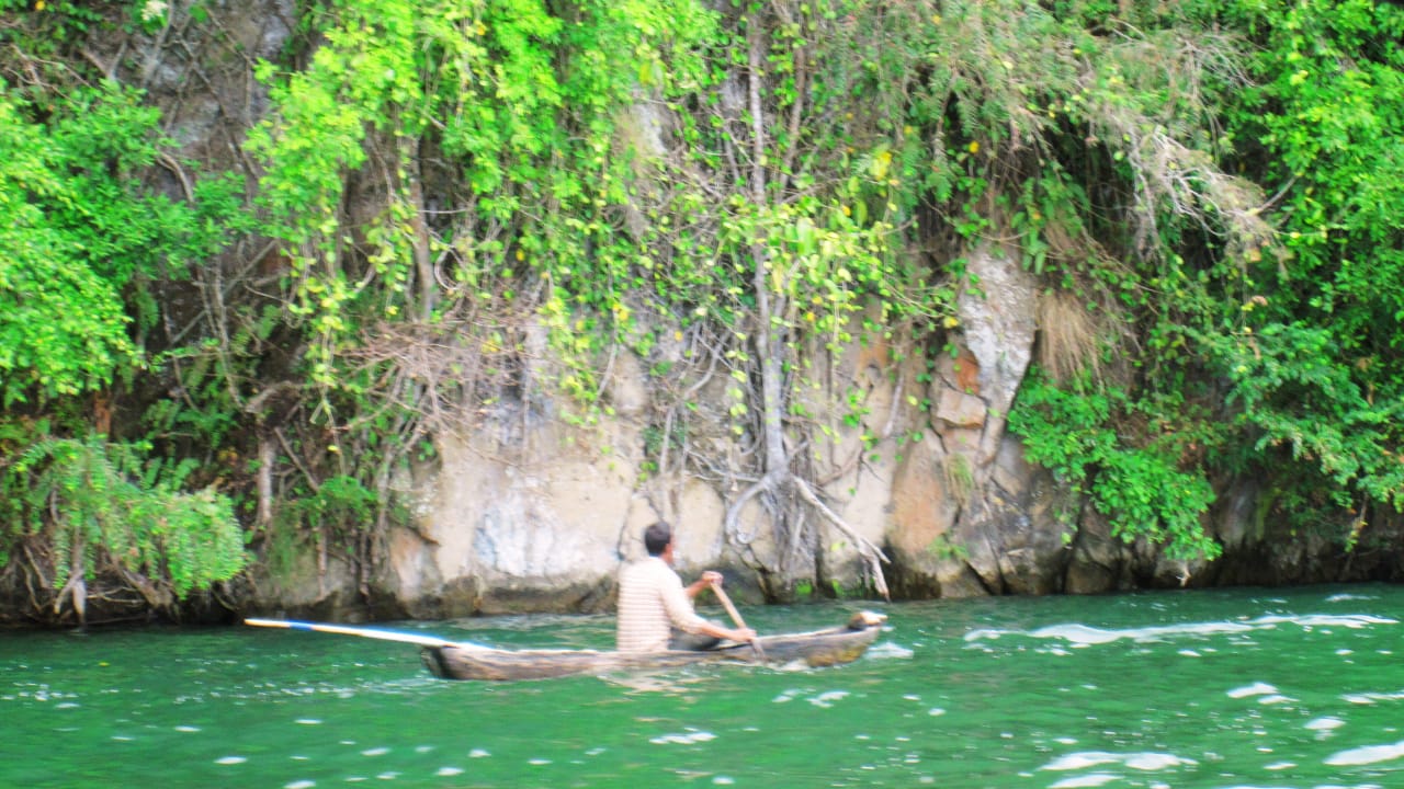 Seorang warga lokal sedang mendayung sampan di Danau Batur, difoto dari belakang dengan panorama alam.
