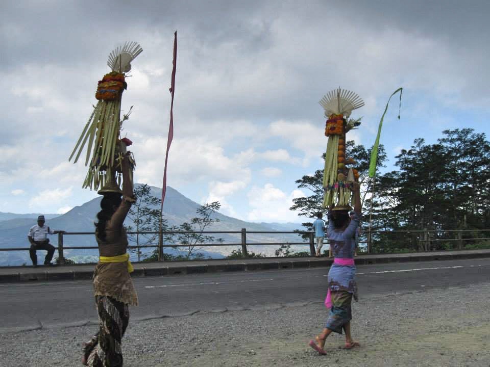 Wanita lokal Bali membawa Gebogan (persembahan/sesajen) di atas kepala (tradisi Nyunggi) saat perjalanan di Kintamani, menunjukkan keanggunan budaya lokal.